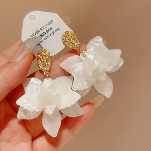 Close-up of elegant white flower earrings with silver needle and gold textured stud