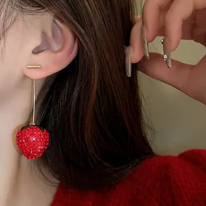 Detailed view of a sparkling red rhinestone strawberry earring with golden bar stud