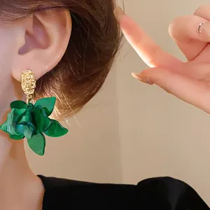 Close-up detail of fresh green flower stud earrings with elegant gold textured base on ear