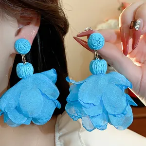 Dettaglio di orecchini a fiore in rafia e chiffon blu vibrante indossati da una modella