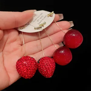 Detailed close-up of sparkling crystal strawberry and glossy red cherry drop earrings