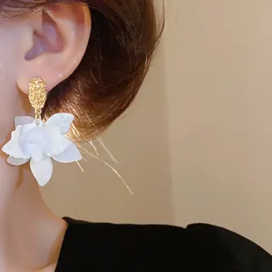 Detailed view of elegant white flower petal earrings with textured gold studs on ear.