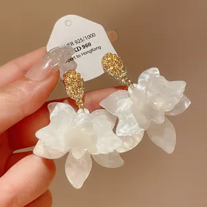 Detailed macro view of elegant white acetate flower earrings with golden textured studs.