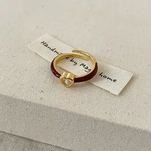 Vue détaillée d'une bague coeur dorée avec émail rouge et une pierre brillante claire.