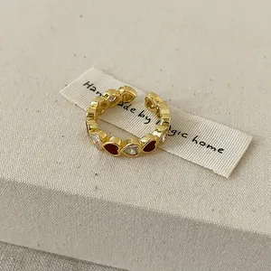 Gros plan d'une bague ouverte dorée avec des détails de cœur en émail rouge et cristal.