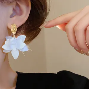 Detailed view of elegant white flower earrings with gold textured studs on ear