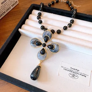 Vintage-style black beaded necklace with a large marble-textured flower pendant and teardrop detail.