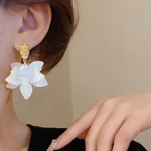 Detailed shot of white layered petal earrings with textured gold studs on model