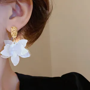 Detailed view of elegant white flower earrings with gold textured studs worn on the ear.
