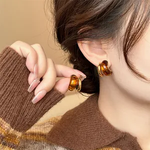 Primer plano de pendientes de aro en forma de C de resina ámbar con diseño retro Maillard.