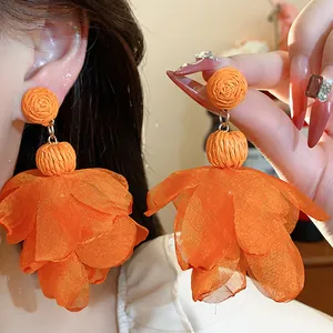 Primo piano di orecchini a fiore in rafia e chiffon arancione brillante per le vacanze