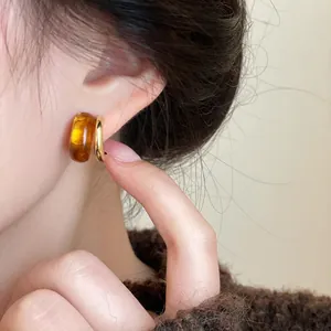 Primer plano de pendientes en forma de C de resina ámbar y metal dorado en modelo.