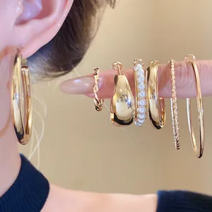 Detailansicht eines eleganten goldenen Ohrring-Sets mit Reifen und Perlen am Finger
