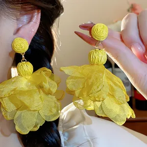 Dettaglio di orecchini a fiore in rafia e chiffon gialli su una modella