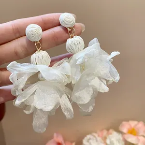 Dettaglio di orecchini a fiore in chiffon bianco con perline di rafia e perla centrale