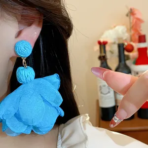 Dettaglio di orecchini a fiore in rafia e chiffon blu brillante indossati dalla modella