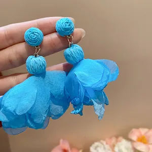 Vista dettagliata di orecchini pendenti con fiori in rafia blu e petali di chiffon