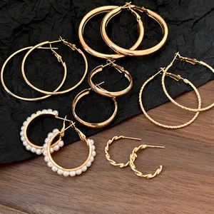 Set mit verschiedenen goldenen Creolen mit Perlenakzenten und gedrehten Designs auf Holzoberfläche.