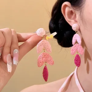 Detailed macro view of pink hand-woven raffia drop earrings worn on a model's ear