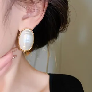 Detailed close-up of elegant oval pearl earrings with gold plating worn by an Asian model