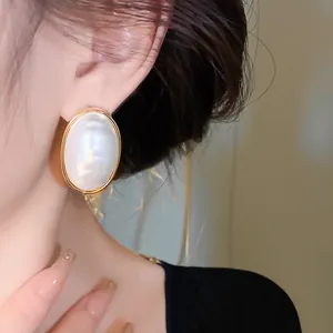 Close-up of gold-plated oval pearl earrings worn on ear, showing minimalist elegant style.