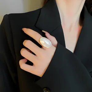 Detail of an elegant gold-plated ring with an oval pearl-like stone worn on a finger.