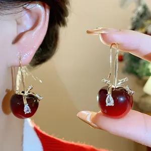 Detailaufnahme eleganter roter Harzapfel-Ohrringe mit Zirkon-Schleife und Goldhaken