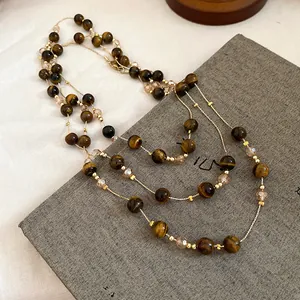 Detailed close-up of vintage tiger eye beaded layered necklace on grey texture background