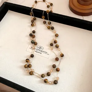 Close-up detail of a vintage tiger eye beaded necklace with gold chain on a display tray
