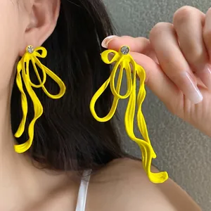 Vibrant yellow oversized wavy bow earrings with sparkling rhinestone studs on ear