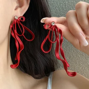 Elegant red ribbon bow earrings with sparkling rhinestone studs worn by Asian model