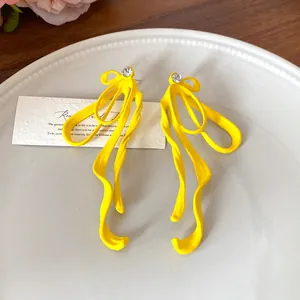 Detail view of vibrant yellow bow earrings with flowing ribbon design and crystal stud