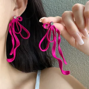 Close-up of bright pink oversized ribbon bow earrings with rhinestone studs on ear