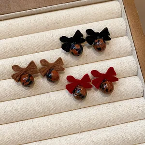 Primo piano di eleganti orecchini a fiocco floccati in nero, marrone e rosso su vassoio.