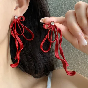 Close-up detail of red ribbon bow earrings with rhinestone studs on model.
