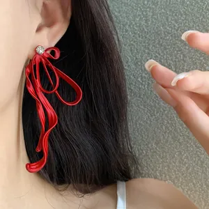Close-up view of elegant red ribbon bow earrings with rhinestone studs worn by a model