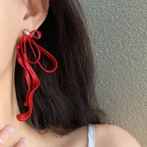 Detailed macro view of red matte ribbon bow earrings with a sparkling rhinestone center.