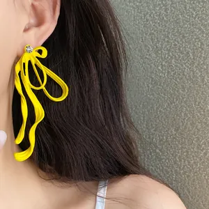 Macro detail of fashionable yellow wavy ribbon bow earrings with sparkling rhinestone accent