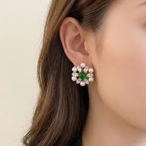 Vintage style floral stud earrings with pearls and green center stone worn by model
