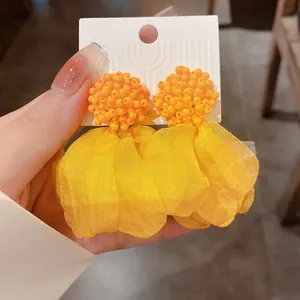 Detailed view of yellow floral drop earrings featuring orange beaded clusters on white card