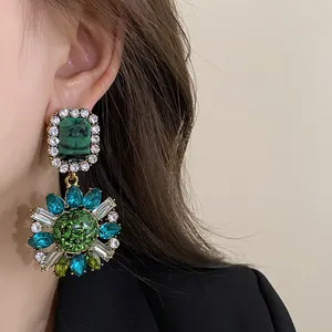 Detailed view of vintage palace style earrings with green emerald and turquoise rhinestones.
