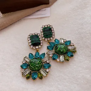 Close-up of vintage court-style earrings with green crystals and floral rhinestone design