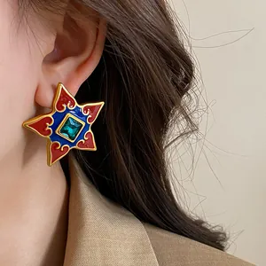 Close-up of vintage palace-style star earrings with colorful enamel and a central green gem