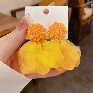 Handheld close-up of vibrant orange beaded and yellow fabric petal drop earrings.