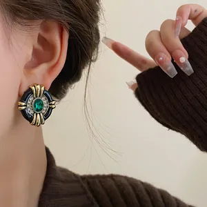 Close-up of vintage palace style gold-tone earrings featuring emerald green gemstone.