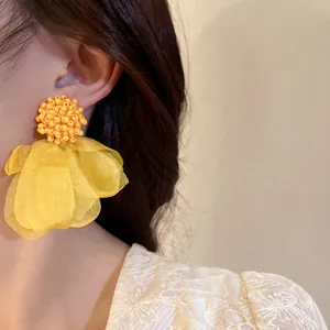 Detailed macro view of yellow floral fabric petal earrings with intricate beaded cluster.
