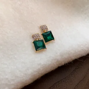 Detailed close-up of vintage style emerald green square stud earrings on soft cream knit fabric