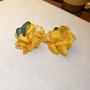 Close-up of yellow mesh flower stud earrings with delicate layered fabric petals.