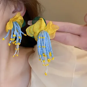 Detail of vibrant yellow mesh flower earrings with blue beaded tassels on model's ear