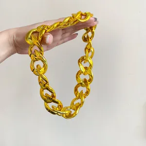 Detailed view of a chunky gold acrylic chain necklace in punk style being held.